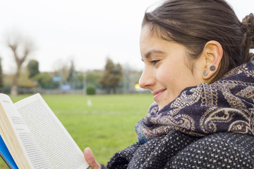 Happy young woman sitting at a bench in a park waiting and reading a book. Medium close up shot.