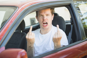 Junger Mann sitzt im Auto und zeigt den Mittelfinger / Vogel