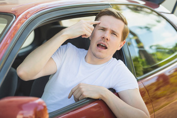 Junger Mann sitzt im Auto und zeigt den Mittelfinger / Vogel