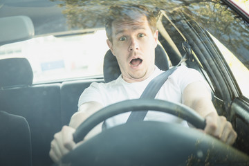 Junger Mann sitzt im Auto und ist schockiert