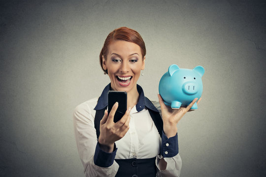 happy young woman holding piggy bank looking at smart phone
