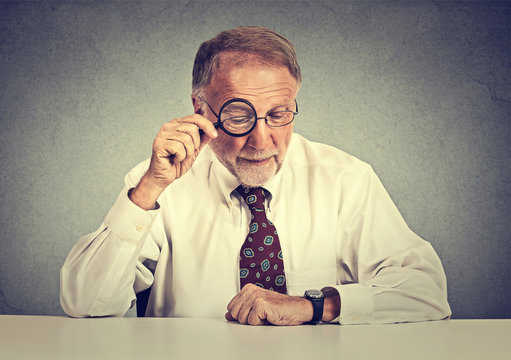 Senior business man looking through a magnifying glass sitting at office desk