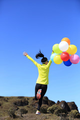 young cheering woman running with colorful balloons on mountain peak
