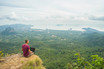 Fototapeta na wymiar Man working with laptop sitting on the rocky mountain on beautiful scenic clif background. Thailand. Krabi .
