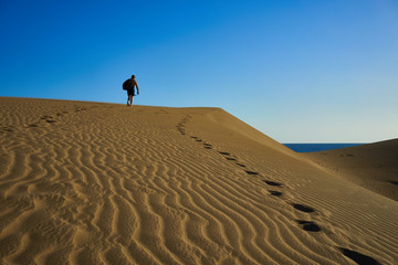 Lost man on sandy dunes in desert / Sandy and wavy dunes with stylish forms in a wide desert under blue sky