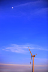 Wind turbine at dawn with the Moon in blue sky