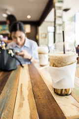 cup of Ice Caramel Macchiato and ice cappuccino on the wooden table and blurry asia woman background