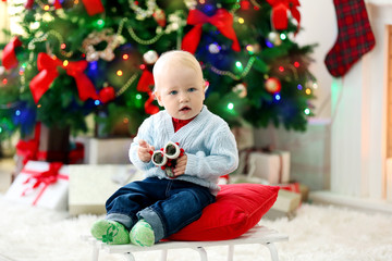 Obraz na płótnie Canvas Funny baby sitting on sledge and Christmas tree and fireplace on background