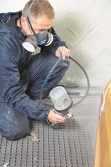 Body painter with airgun spraying paint on car