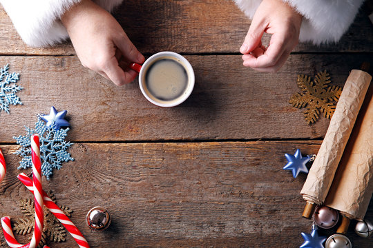 Christmas concept. Santa takes cup of coffee in hands on wooden background, close up