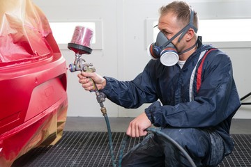 Body painter with airgun spraying red paint on car