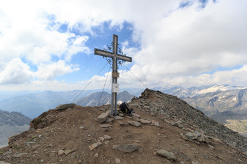 Fototapeta na wymiar Summit cross and backpack on mountain Weißspitze with panorama in Hohe Tauern Alps, Austria