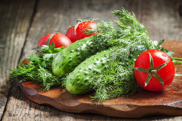 Fresh cucumbers, tomatoes, dill and parsley on the old wooden ba