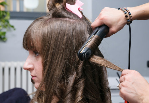 Ragazza dal parrucchiere che arriccia i capelli, fuoco selettivo