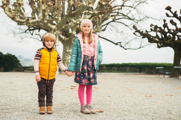 Outdoor portrait of two kids, little girl and her brother, wearing warm colorful jackets