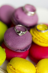 Fototapeta na wymiar Два обручальных кольца и кольцо для помолвки на тарелке яркими пирожными