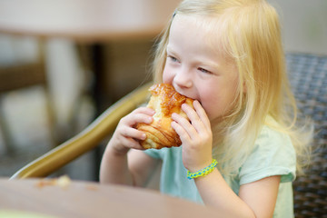 Adorable little girl eating a bun in an outdoor cafe