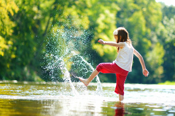 Cute little girl having fun by a river on warm summer day - Powered by Adobe