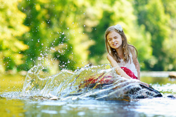Cute little girl having fun by a river on warm summer day