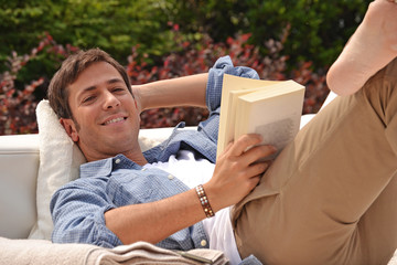 Hombre relajado recostado leyendo un libro en la piscina de su casa. - obrazy, fototapety, plakaty