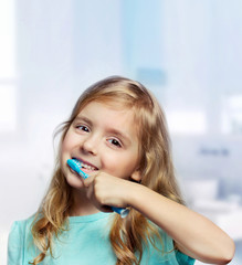 Child girl toddler cleaning teeth in bathroom background.