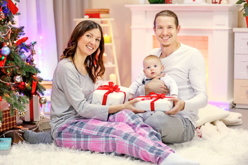 Happy parents with baby near Christmas tree on the floor in the decorated room