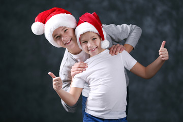 Brothers in Santa hats on grey background