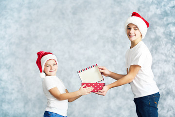 Obraz premium Brothers in Santa hats with gift box on grey background