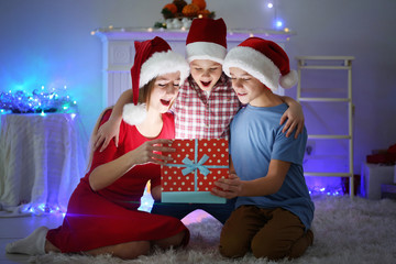 Obraz premium Happy sister and brothers open gift box on the floor in decorated Christmas room