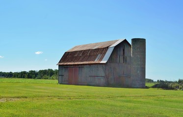 Weathered wooden vintage barn with silo and surrounding farmland