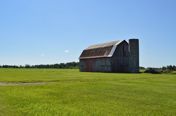 Obraz premium Weathered wooden vintage barn with silo and surrounding farmland