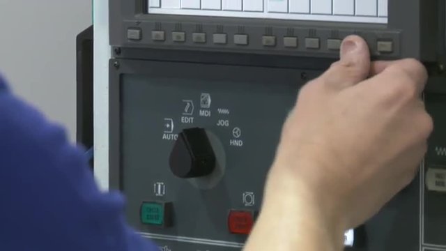 Close up of worker's hands operating the computer controls on a CNC lathe.  Tilt up to screen.