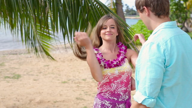 Young man putting lei garland of pink orchids around woman neck at beach Oahu, Hawaii.