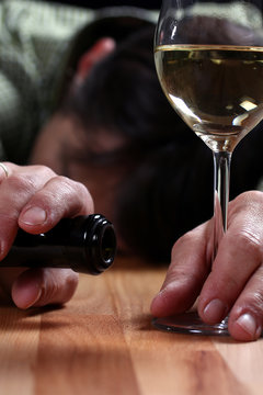 Alkoholiker schläft auf Tisch, hält noch Flasche und Glas in der Hand