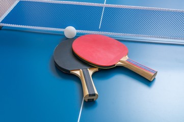 Ping pong rackets with net on blue table.