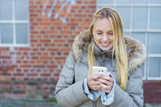 glückliche junge frau schaut draußen auf ihr smartphone