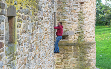 Mann klettert eine Burgmauer hinauf.