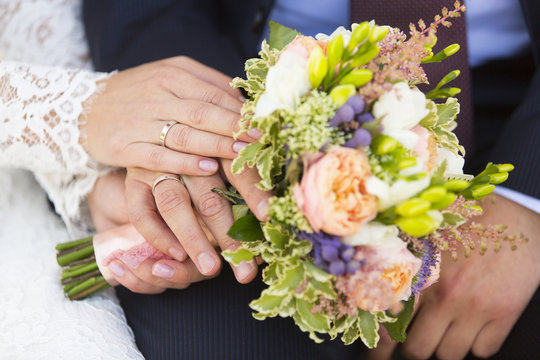 Руки жениха и невесты с обручальными кольцами на свадебном букете 
