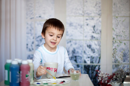 Cute little preschool boy, drawing picture on mug for his father