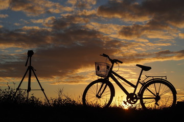 Obraz premium A tripod and a bicycle on country road in the evening: silhouette photo