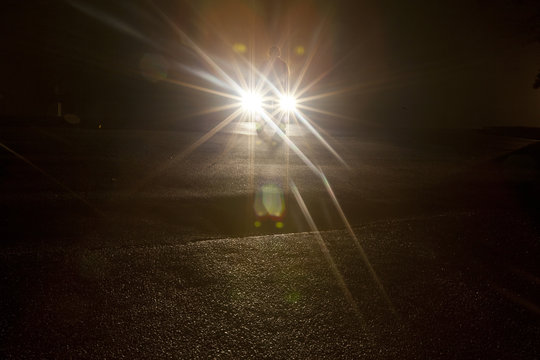 A shadowy figure standing in front of vehicle headlights in the dark of night.