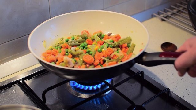 Mixed vegetables in frying pan cooking, vegetarian meal being prepared at home in kitchen