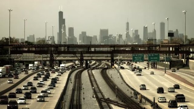 High contrast view of freeway traffic and commuter rail transit system with the city of Chicago in the background.  Originally recorded in 4K, Ultra High Definition.