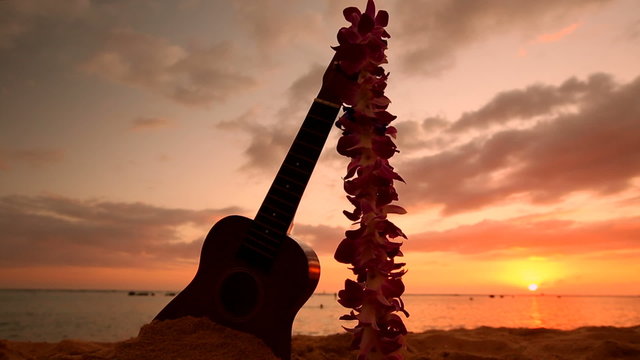 Traditional Hawaiian instrument Ukulele and flower wreath or garland lei on sandy beach at sunset Oahu Hawaii.