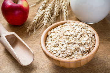 Ingredients for porridge: rolled oats (oat flakes), milk and red apple on rustic wooden background. Healthy lifestyle concept