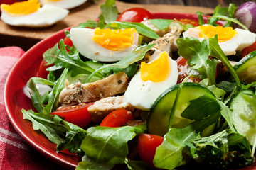 Fresh salad with chicken, tomatoes, eggs and arugula on plate