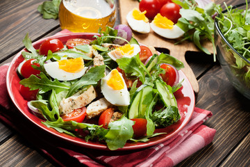 Fresh salad with chicken, tomatoes, eggs and arugula on plate
