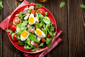 Fresh salad with chicken, tomatoes, eggs and arugula on plate