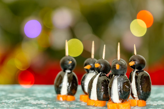 Penguins made of black olives, carrots and feta cheese, against festive background