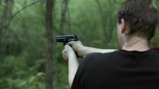 Over the shoulder view of man firing a .44 caliber pistol in woodland.  Muzzle flashes visible.  Recorded in 4K, Ultra High Definition.